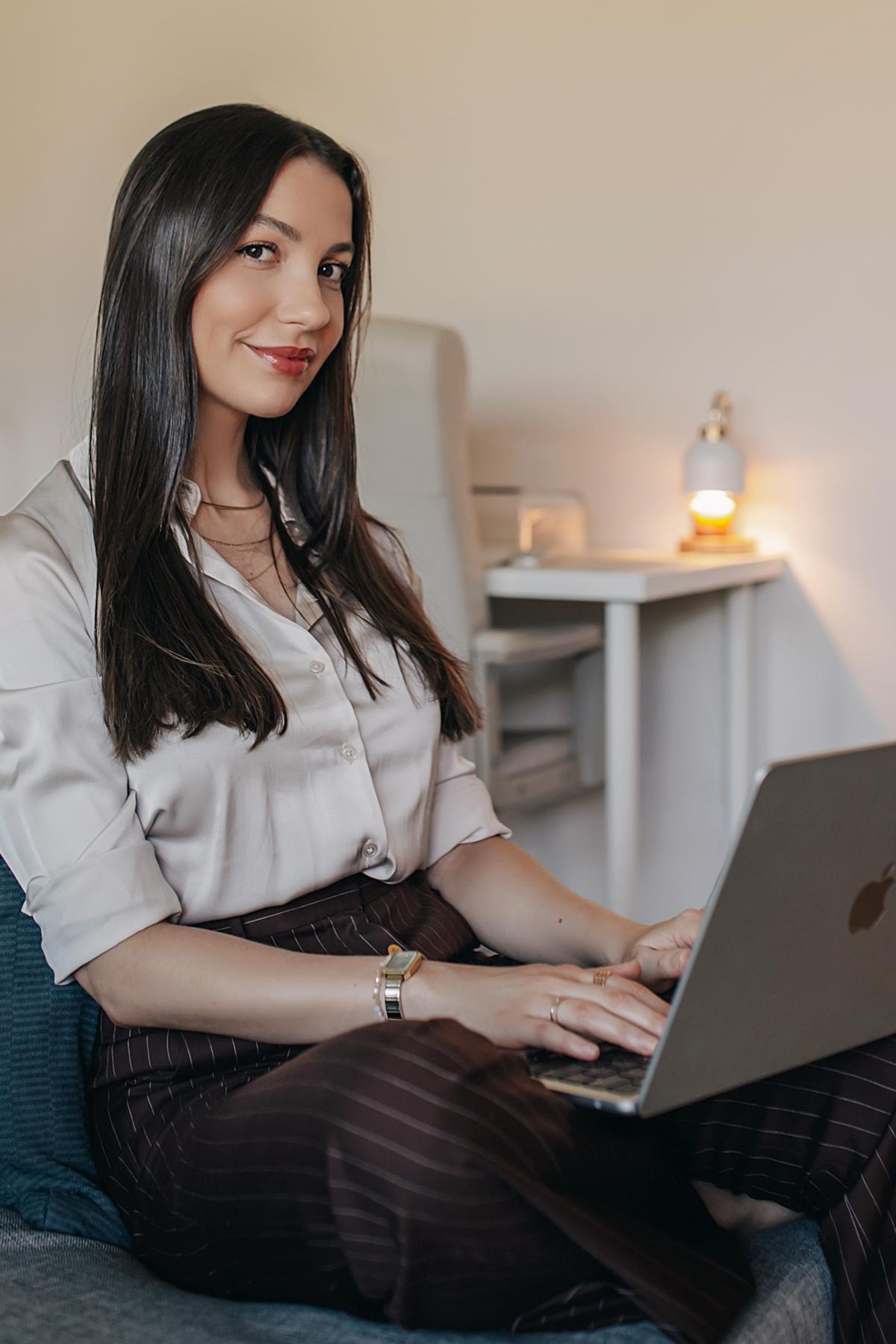 Aline Delamare trabalhando no notebook, sentada em uma poltrona